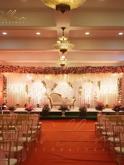 A gorgeous reception stage with hues of orange and red. The floral backdrop and candle-lit aisle create a warm, elegant, and chic atmosphere.