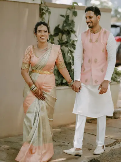Here is an example of subtle and elegant couple coordination. The groom wears a simple white kurta and pants, elevated by a custom-made light pink Nehru jacket with delicate gold embroidery that complements his partner's saree.