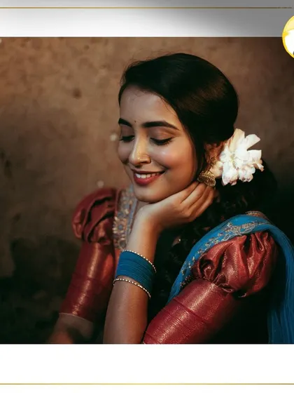 A serene and classic bridal portrait. The makeup features a soft red lip and defined eyes, beautifully complemented by the traditional puff-sleeve blouse and fresh flowers in her hair.