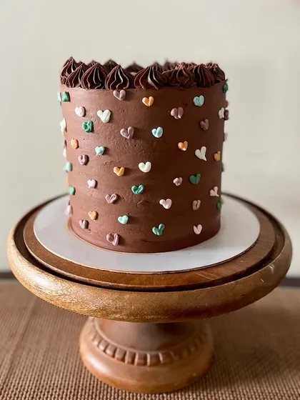 A tall chocolate cake that's as cute as it is delicious. The rich chocolate buttercream is covered in tiny, multi-colored piped hearts, making it a sweet and simple design for any birthday.