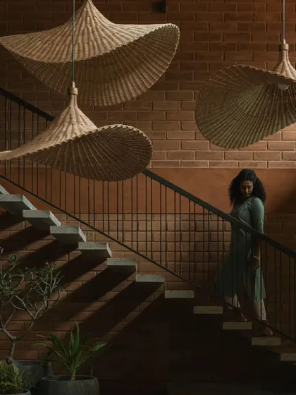 A detail of the floating staircase at Villa Maati. The design features cantilevered stone steps against an exposed brick wall, with sculptural bamboo pendant lights that create dramatic shadows and highlight the material textures.