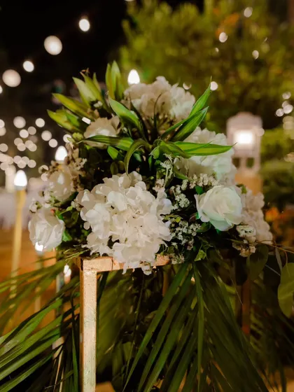 A beautiful floral arrangement of white lilies and hydrangeas on a gold stand, set against a backdrop of soft bokeh lights. This kind of detail adds a layer of sophistication and elegance to any event space.