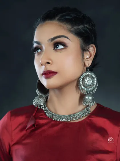 A close-up beauty shot focused on traditional silver jewelry. The rich red top and dark background make the intricate details of the earrings and necklace stand out.
