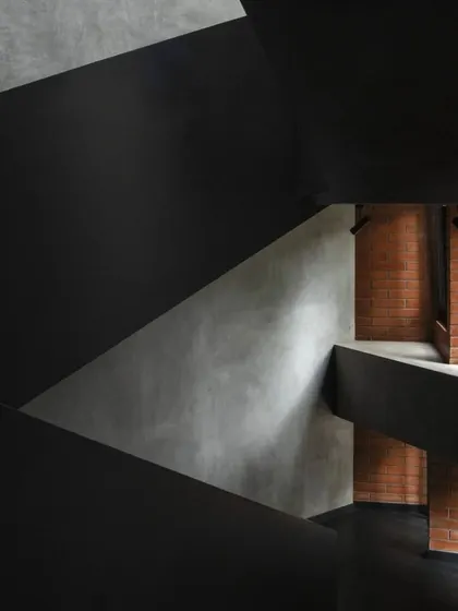 A detail of the Brick House staircase, showing the contrast between the smooth, dark plaster and the rough texture of the adjacent brickwork.