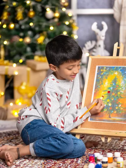 Christmas is about opening our hearts. A young boy is completely absorbed in painting a beautiful Christmas tree scene.
