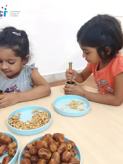 Two girls work together, using mortars and pestles to grind walnuts. This collaborative activity fosters teamwork and communication.