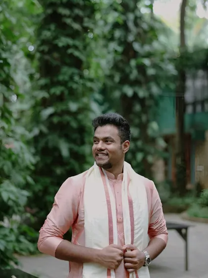 A candid portrait of the groom, smiling as he looks off-camera. Dressed in a traditional pink kurta, this shot captures his relaxed and happy demeanor during the wedding celebrations.