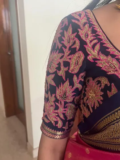 A close-up of the intricate pink and gold floral embroidery on the navy blue blouse sleeve.