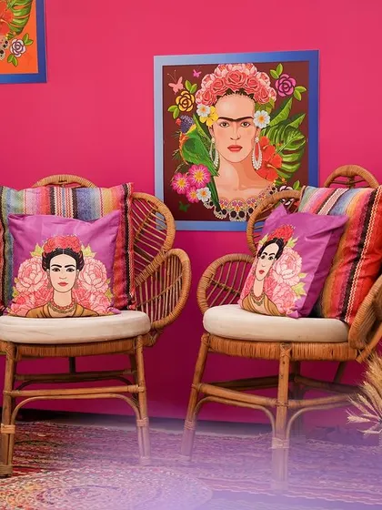 Another view of the Frida Kahlo photo booth, showcasing the vibrant pink wall and the collection of artistic portraits. The rattan peacock chairs add a touch of bohemian flair.
