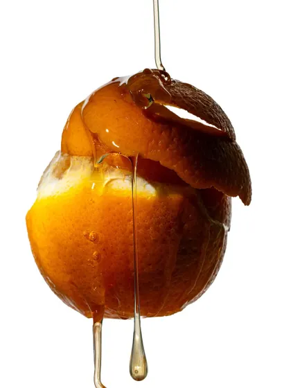 An abstract shot of a peeled orange with honey dripping down. This image focuses more on form and texture, exploring the relationship between the rough peel, the soft fruit, and the smooth liquid.