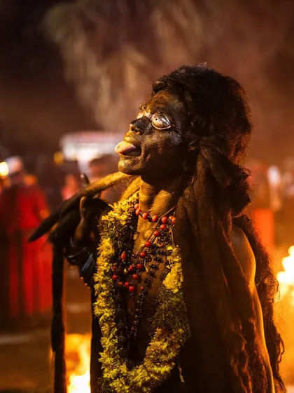 A devotee with his face painted black and tongue out, channeling a fierce deity during Kulasai Dasara. The fire in the background adds to the intensity of the moment.