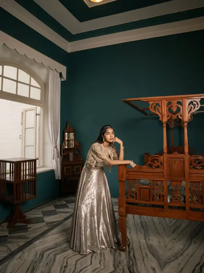An environmental portrait from a brand campaign, shot in a heritage location. The composition uses the room's architecture to frame the model and the shimmering outfit.