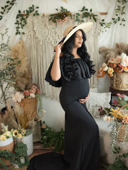 A beautiful full-length shot showing the elegant silhouette of the black maternity gown against the detailed boho backdrop.