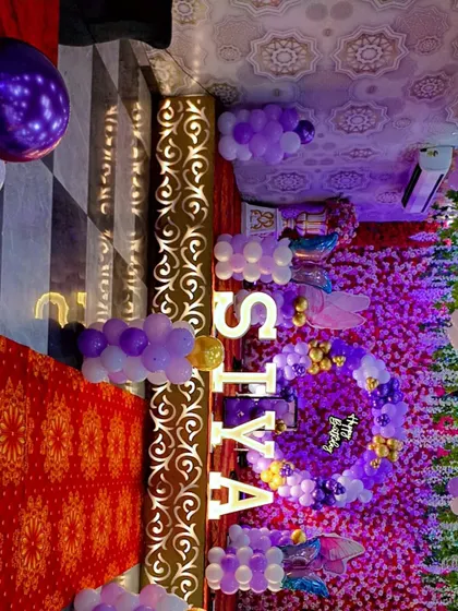A grand stage setup for Siya's first birthday, featuring a massive flower wall backdrop and purple and white balloon decorations.