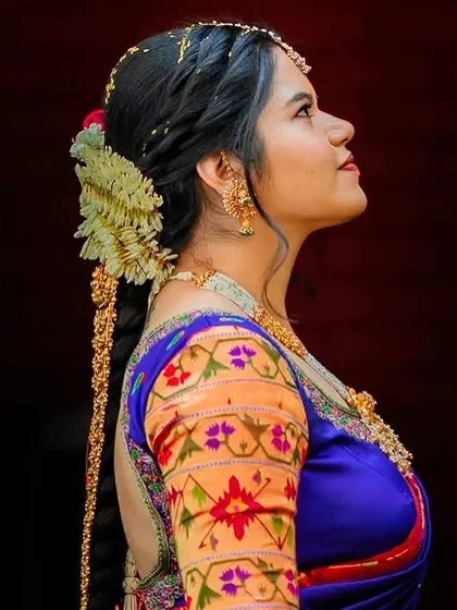 A profile shot of a bride, highlighting the traditional South Indian hairstyle with a long braid and fresh flowers. The rich colors of her saree stand out against the dark background.