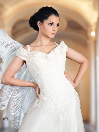 A creative portrait with the model in a white gown, with large white feathers suggesting angel wings. The background adds to the ethereal, dreamlike quality of the shot.