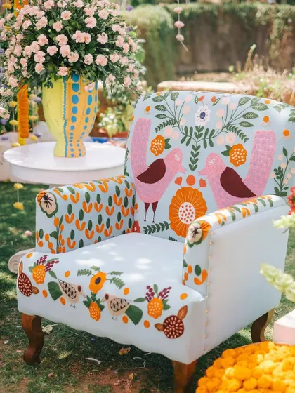 A whimsical, custom-embroidered armchair becomes an installation in its own right. Surrounded by baskets of marigolds and a vase of colorful blooms, it creates a perfect corner for photos and relaxation.