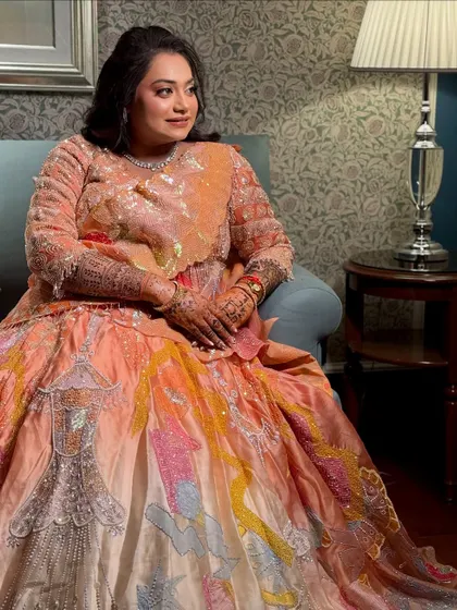 The bride seated, showing off her unique and artistic sangeet lehenga, complemented by soft, elegant makeup.