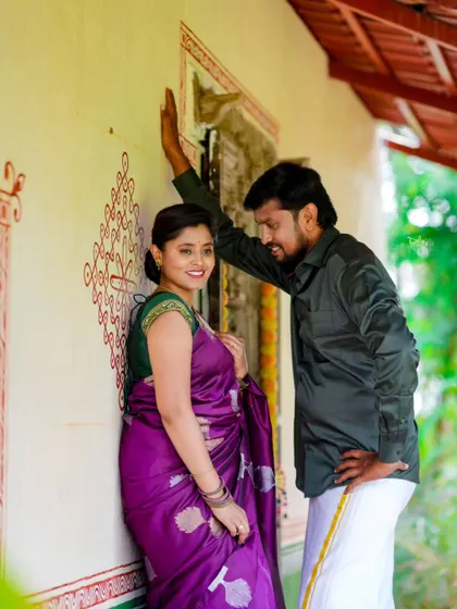A romantic pre-wedding photo with a rustic, village-like background. The traditional outfits and setting create a unique, earthy feel.
