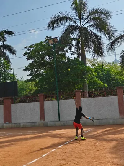 A player tossing the ball for a serve against the backdrop of our academy's palm trees. We train in all conditions to prepare for real tournament environments.