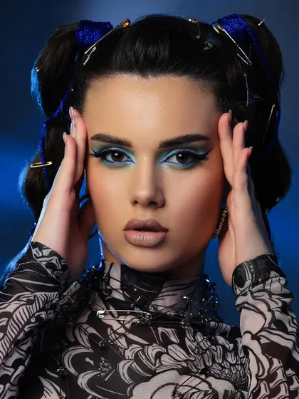 A wider shot of the safety pin look, showing how the accessories and makeup come together with the printed top. The blue background enhances the cool tones of the makeup.