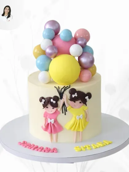 A delightful cake celebrating twin sisters. This design features two adorable, handcrafted figures holding a cascade of colorful balloon-like spheres, with their names written at the base.