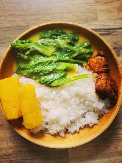 A simple, everyday meal plate with a North-Eastern touch. It includes rice, mustard leaves cooked with dal, fried chicken, and crispy fryums.