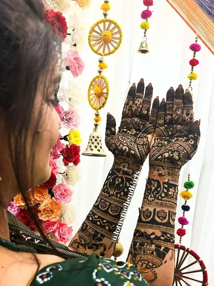 A bride showcasing her full bridal mehendi against a colorful backdrop. The design is a beautiful mix of traditional and contemporary elements.