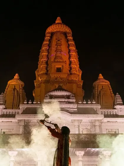 Priests performing the Maha Aarti at JK Temple in Kanpur, with smoke from the diyas creating a mystical atmosphere in front of the temple's grand facade.
