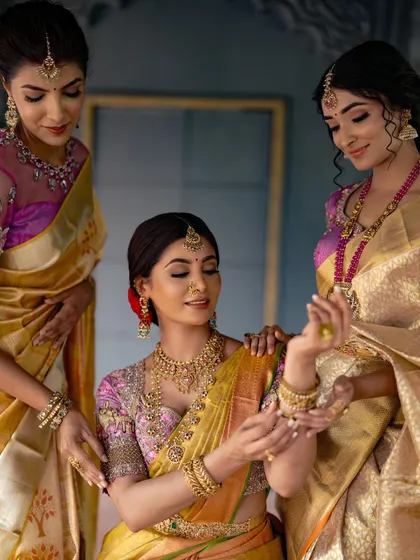 A lovely portrait of a bride with her bridesmaids, all dressed in gorgeous silk sarees, sharing a moment as they admire her jewelry.