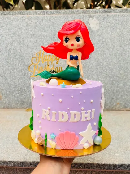 An underwater adventure with this Little Mermaid cake. The lavender buttercream is decorated with fondant seashells, starfish, and an Ariel topper.