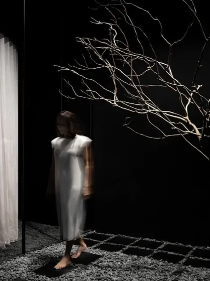 At the entrance, a bare tree stands as a sculptural sentinel. This organic element introduces a sense of stillness and natural texture into the austere, dark environment, setting a meditative tone for the retail experience that unfolds within.
