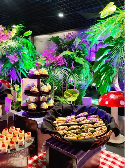 A colourful and whimsical dessert spread from our Spotify tropical grazing table. The display includes mini pastries, donuts, and cupcakes, set against a backdrop of lush greenery and playful decor.