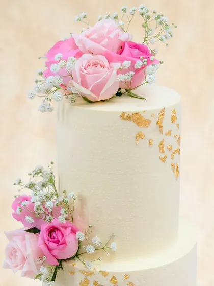 A close-up of the top tier, showcasing the beautiful arrangement of fresh pink roses and the subtle texture of the buttercream, dotted with gold.