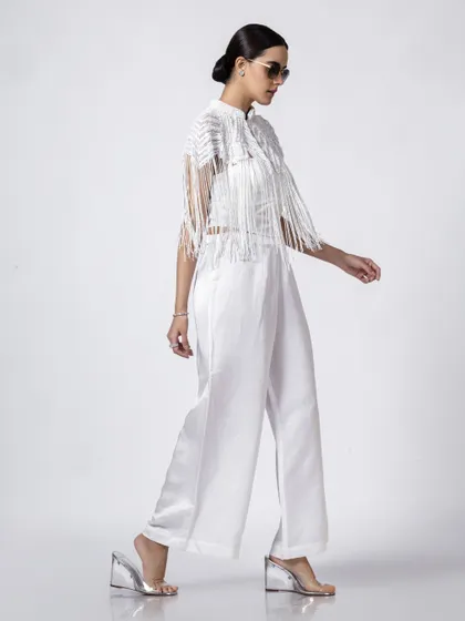 A model in a stylish white outfit with a fringe jacket, shot in profile to highlight the unique silhouette and texture of the design.