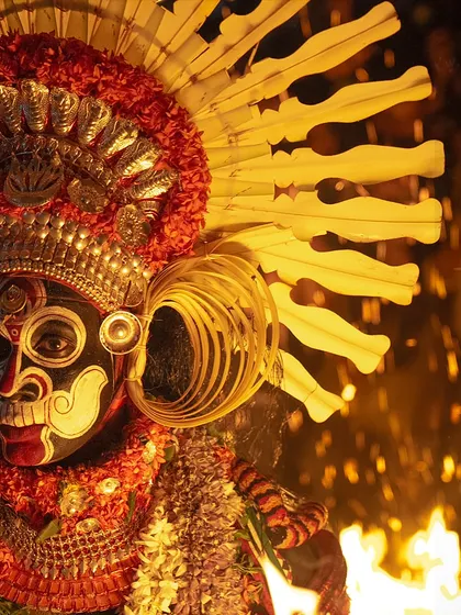 An intimate portrait of the Karim Gullikan Theyyam, with fire sparks flying around his elaborate headgear. This shot highlights the divine and fearsome presence of the performer.