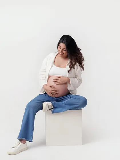 A beautiful, candid-style shot of a mom-to-be in a relaxed, seated pose. Her comfortable jeans and white top create a natural and approachable look for a maternity session.