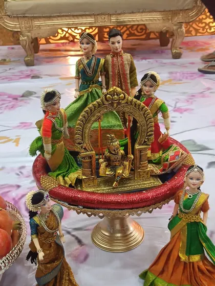 A centerpiece for an engagement featuring dolls representing the family. The main couple is surrounded by other figures, all arranged around a miniature golden swing.