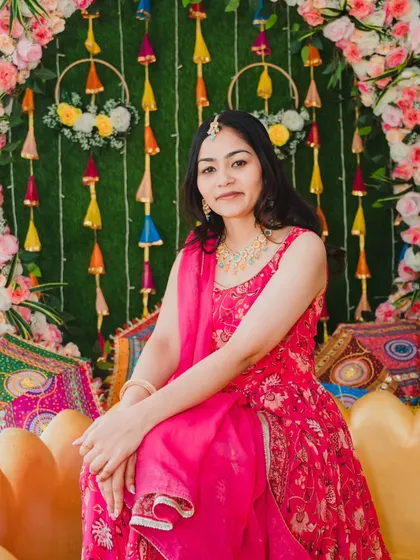 The bride seated against a vibrant, festive backdrop at her Haldi ceremony, looking radiant in her pink outfit.