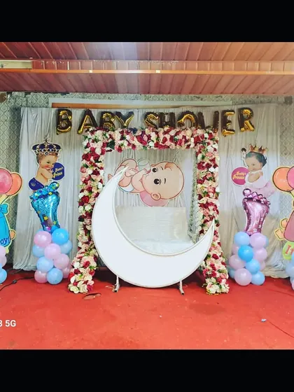 A classic baby shower setup with a floral swing, lighted moon, and 'It's a Boy'/'It's a Girl' props, suitable for any home or small venue.