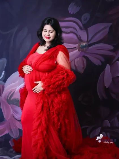 A serene portrait of a mom-to-be in a red ruffled gown, cradling her bump against a painted floral background.