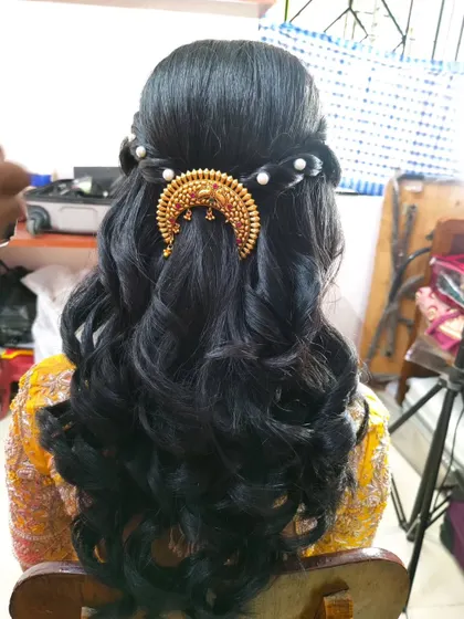 A half-up style with a bouffant and curls, finished with a traditional gold semi-circular hairpiece and pearls.