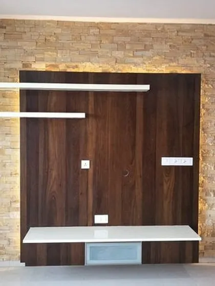 This floating TV unit combines a dark wood back panel with clean white shelves, set against a rustic stone-cladding wall. The backlighting adds depth and highlights the different textures, creating a modern focal point.