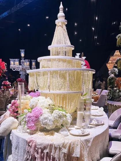 A wider view of the 'Lace Love' table, showing the grand pearl chandelier centerpiece surrounded by lush arrangements of pink and white hydrangeas and roses. The design is a symphony of texture and romance.