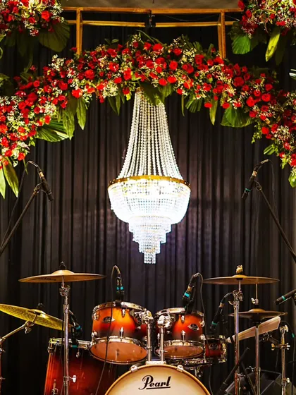 A stunning crystal chandelier hangs beneath a dense arch of red flowers, creating a luxurious focal point above the stage.