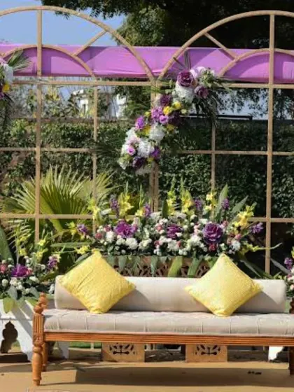 A beautiful Haldi stage with a purple and yellow color scheme. The floral arrangements and elegant sofa create a unique and stylish look.