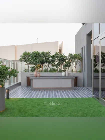 An outdoor bar and counter area on a rooftop terrace, set against a backdrop of trees that provide privacy and a green screen from neighboring buildings. The combination of a manicured lawn and elegant hardscaping makes it ideal for entertaining.