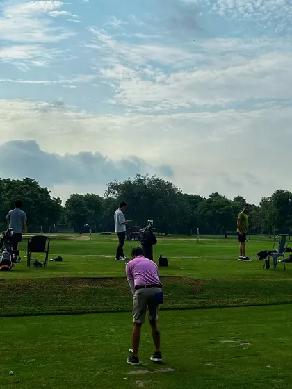 A golfer in a pink shirt stands out against the green, focused on his shot on a busy Saturday.