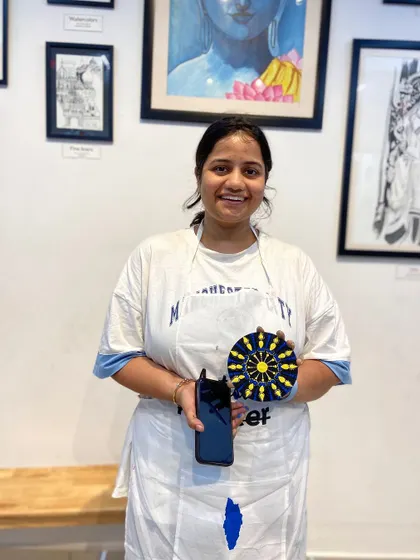 A participant with her finished dot mandala. The bright yellow and intricate design make it a cheerful and eye-catching piece.