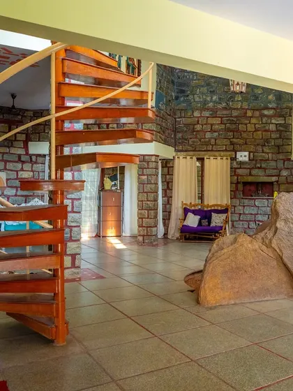 A wide shot of the villa's main hall, showing the spiral staircase and rustic stone columns.